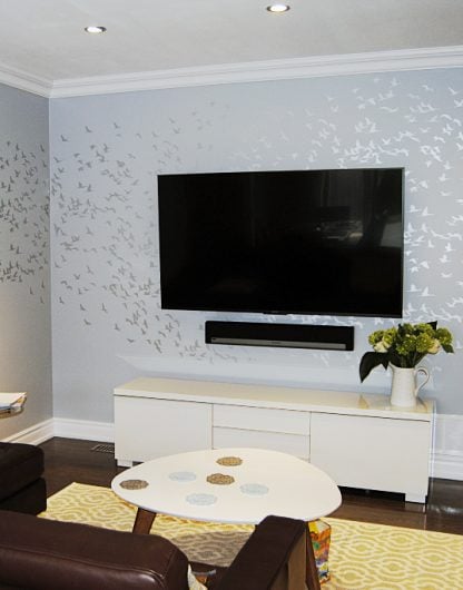 A DIY stenciled accent wall in a living room using the Flock of Cranes birds wall pattern from Cutting Edge Stencils in metallic silver over gray. http://www.cuttingedgestencils.com/bird-flock-wall-stencil-pattern.html