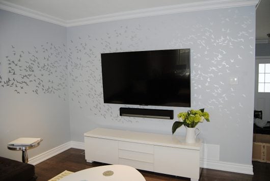A DIY stenciled accent wall in a living room using the Flock of Cranes birds wall pattern from Cutting Edge Stencils in metallic silver over gray. http://www.cuttingedgestencils.com/bird-flock-wall-stencil-pattern.html