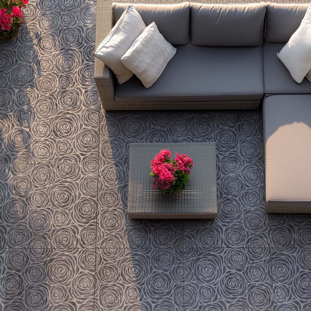 Outdoor cement patio with a gray sectional sofa, coffee table, and pink flowers on a stenciled floor.