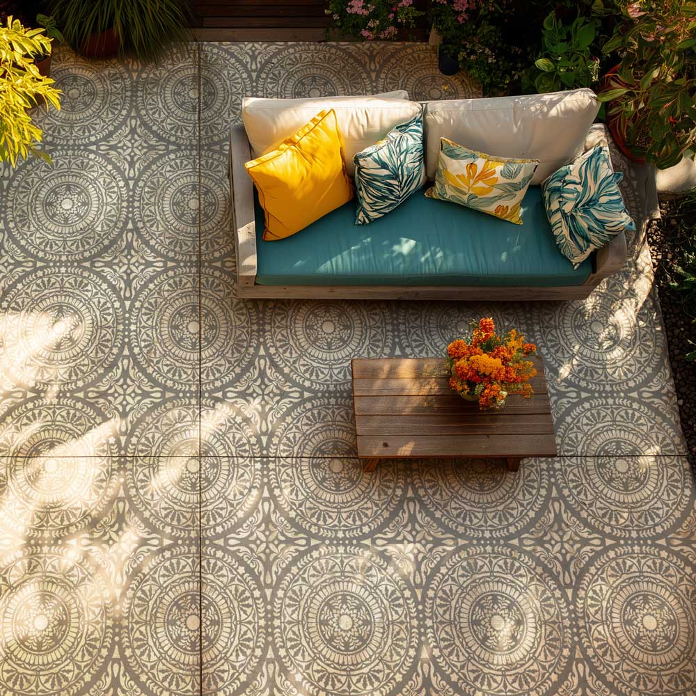 Outdoor seating area with a stenciled cement floor, colorful cushions, and a small table with flowers.