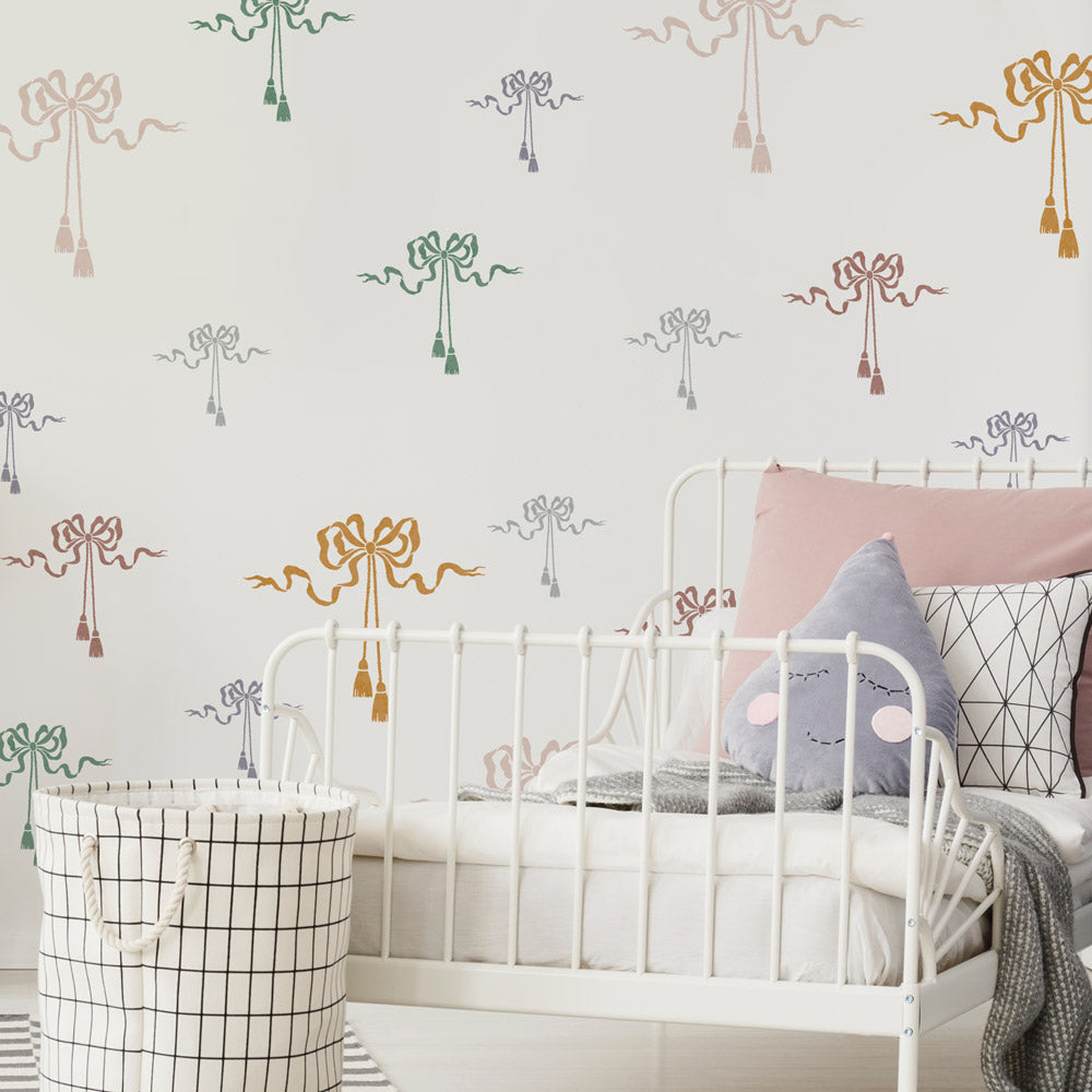 Children's room with white metal bed, patterned silk bow stencils, and storage basket.