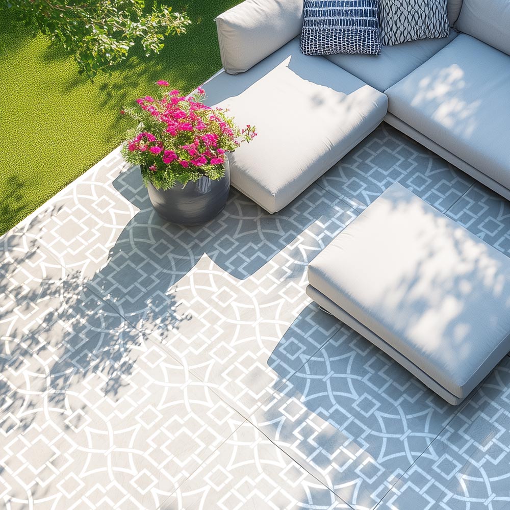 Outdoor seating area with a stenciled cement patio floor, white cushions, and a potted plant.