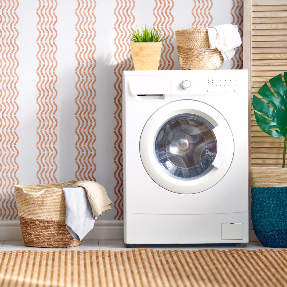White washing machine in a laundry room with wavy stripe wall stencil and decorative elements.