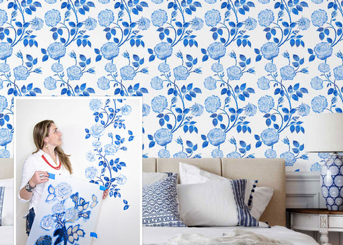 Woman holding a blue floral patterned stencil against a wall with the finished floral design.