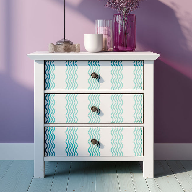 White dresser with wavy patterned stenciled drawers against a purple wall.