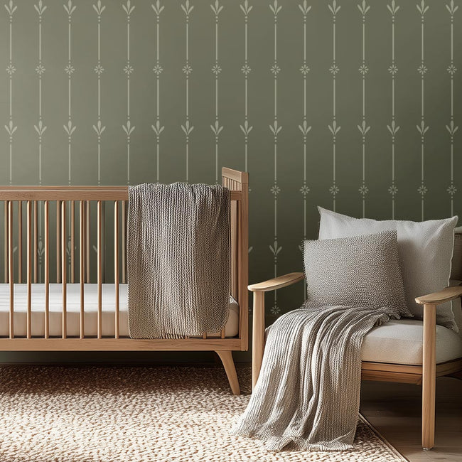 Nursery room with wooden crib and chair against a green wall stencil with decorative pattern.