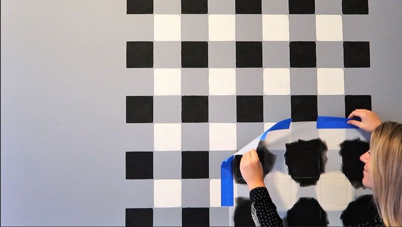 woman painting on grey wall with black and white in a buffalo check pattern