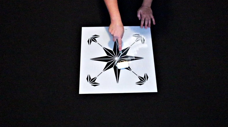woman's hand rolling on white paint over a star shape tile stencil on black floor