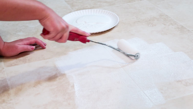 woman's hand rolling primer on beige tile floor with primer paint