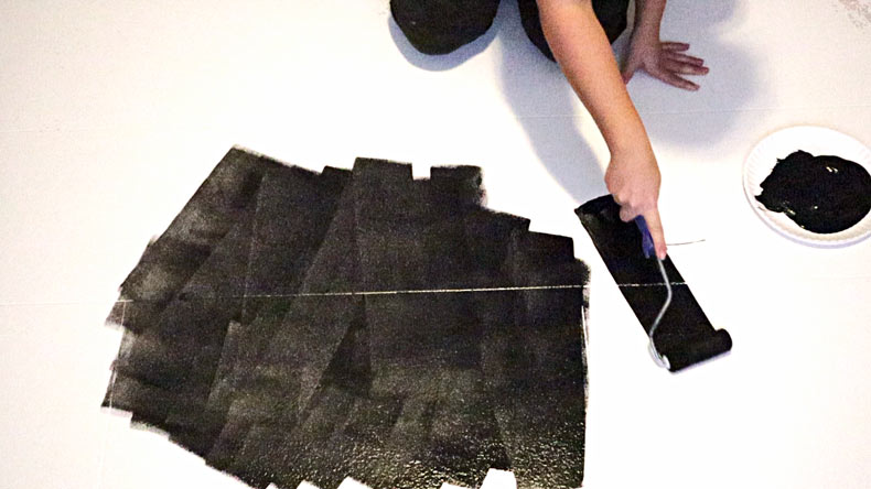 woman rolling black paint on tile floor with dense foam roller 