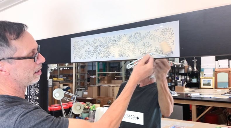 man stenciling inlay pattern a large mirror with white paint