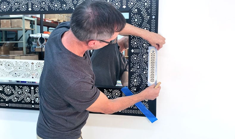 man stenciling inlay pattern on a large hanging mirror 
