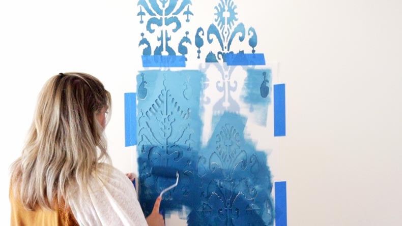 girl rolling blue paint on ikat wall stencil pattern