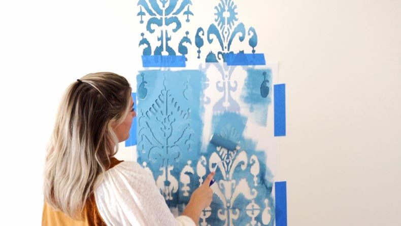girl rolling paint over ikat wall stencil pattern