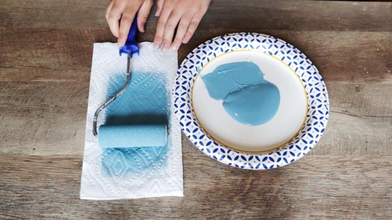 hand on roller for stenciling with blue paint in a plate 