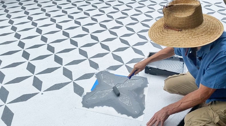 man stenciling faux tiles on cement patio