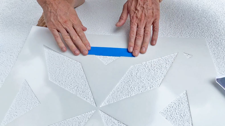 man putting tape over tile stencil
