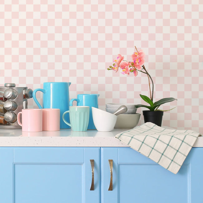 Kitchen counter with colorful mugs, a pitcher, and a plant against a pink checkered wall.
