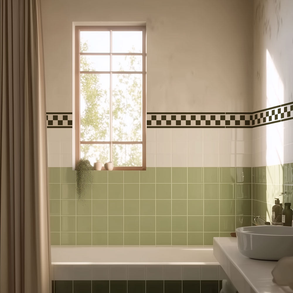 A bathroom interior with a white tub, a white sink and basin, light green square wall tiles, a black-and-white checkered border stripe stencil, a beige curtain, and a window above the tub.