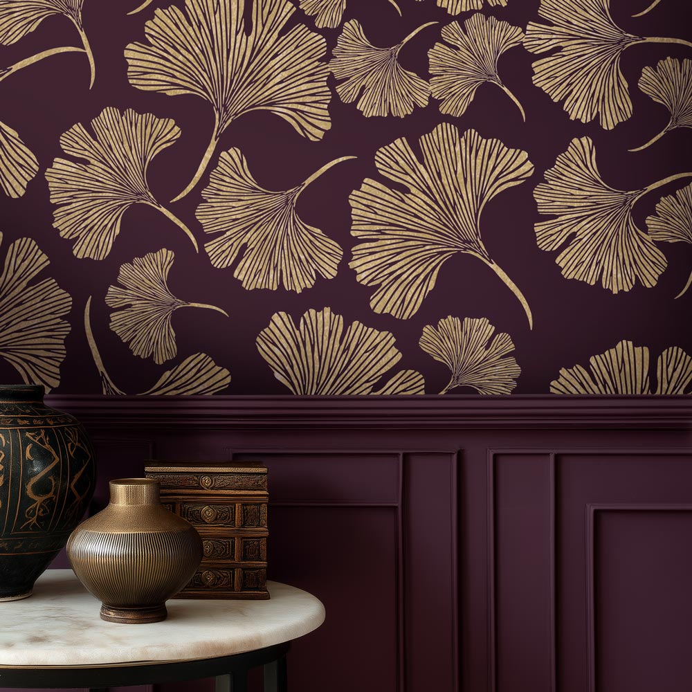 Chinese ginkgo Wall stencil with gold leaf pattern on a dark purple wall, with decorative items on a table below.
