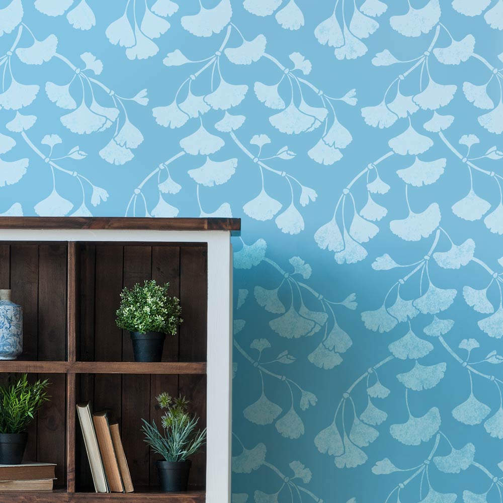 Wallpaper with ginkgo branch pattern on a blue background, wooden shelf with plants and books below.