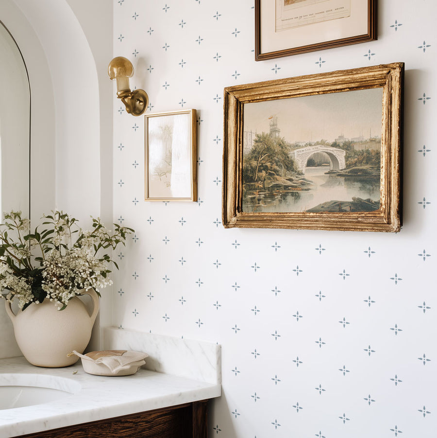 Decorative interior with framed artwork, a vase of flowers, and wall sconce on a stenciled wall.