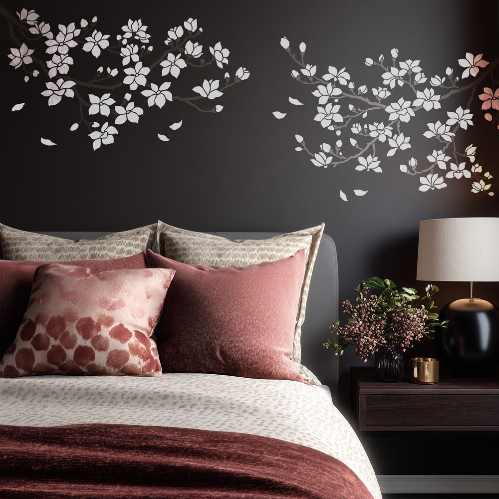 Decorative floral magnolia branch wall stencil on a dark wall above a bed with patterned pillows.