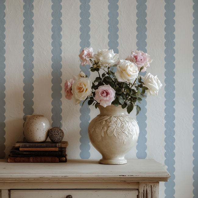 Decorative vase with flowers on a wooden surface against a striped stenciled wall.