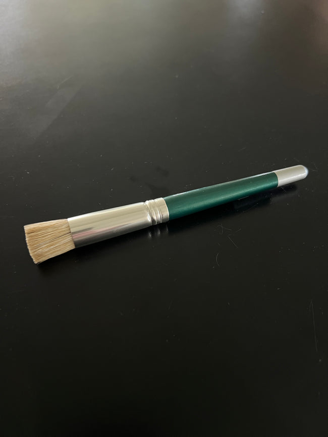 Paintbrush with green handle and beige bristles on a black surface