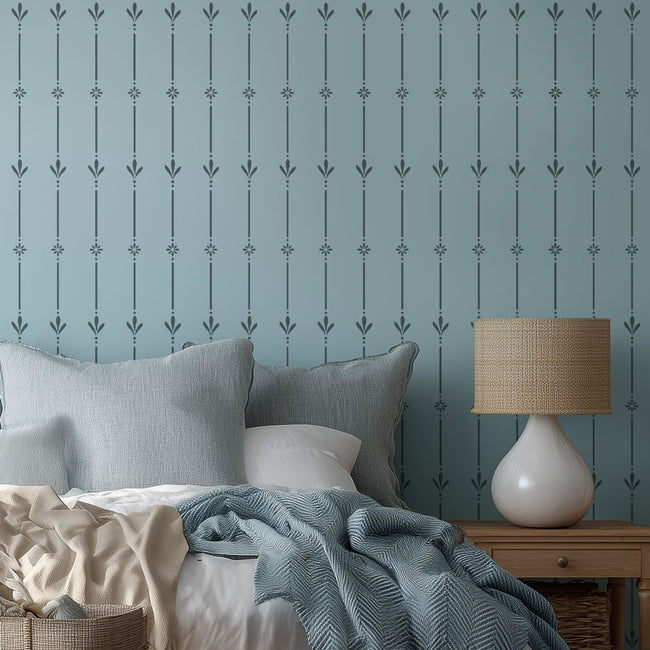 Bedroom with patterned wall stencil, bed with pillows and blankets, and a lamp on a nightstand.